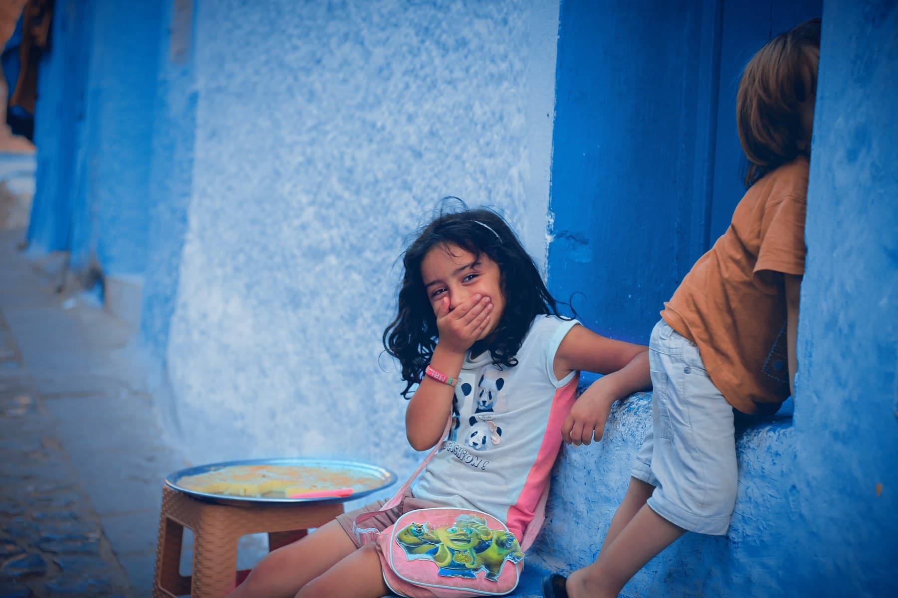 Deux enfants qui rient devant un mur bleu, dans une médina marocaine
